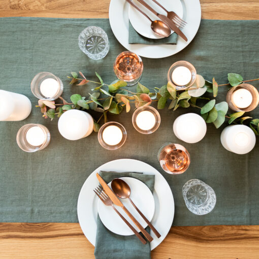 Tischsetting mit Tischwäsche aus Leinen in der Farbe Eukalyptus: Servietten und Tischläufer; dazu in der Mitte Permanent Kerzen und Windlichter mit Maxiteelichtern.