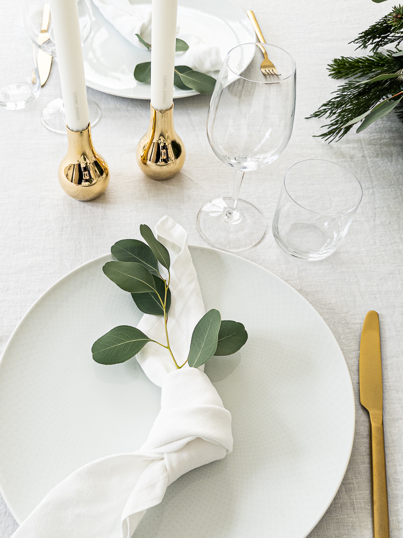 Tischdeko zu Weihnachten in Weiß mit weißer Leinentischdecke und Leinenservietten in Weiß. Goldene Kerzenleuchter von Georg Jensen und Deko mit Eukalyptus.